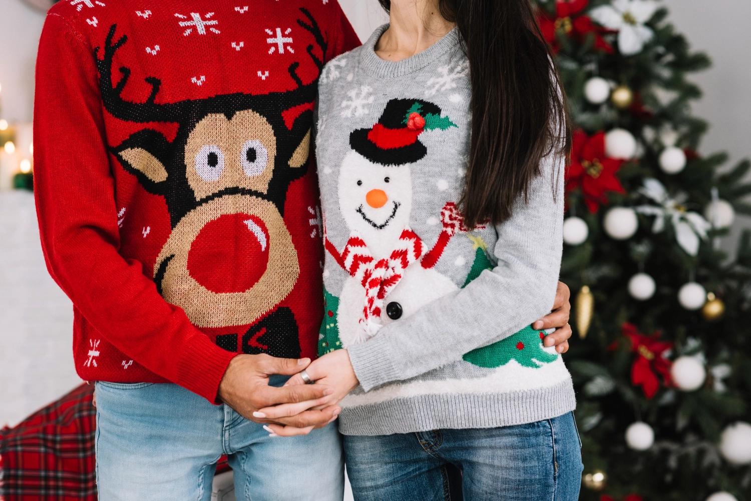 A couple wearing matching Christmas sweaters, one with a reindeer, the other with a snowman, which is one of the best Christmas traditions for couples.