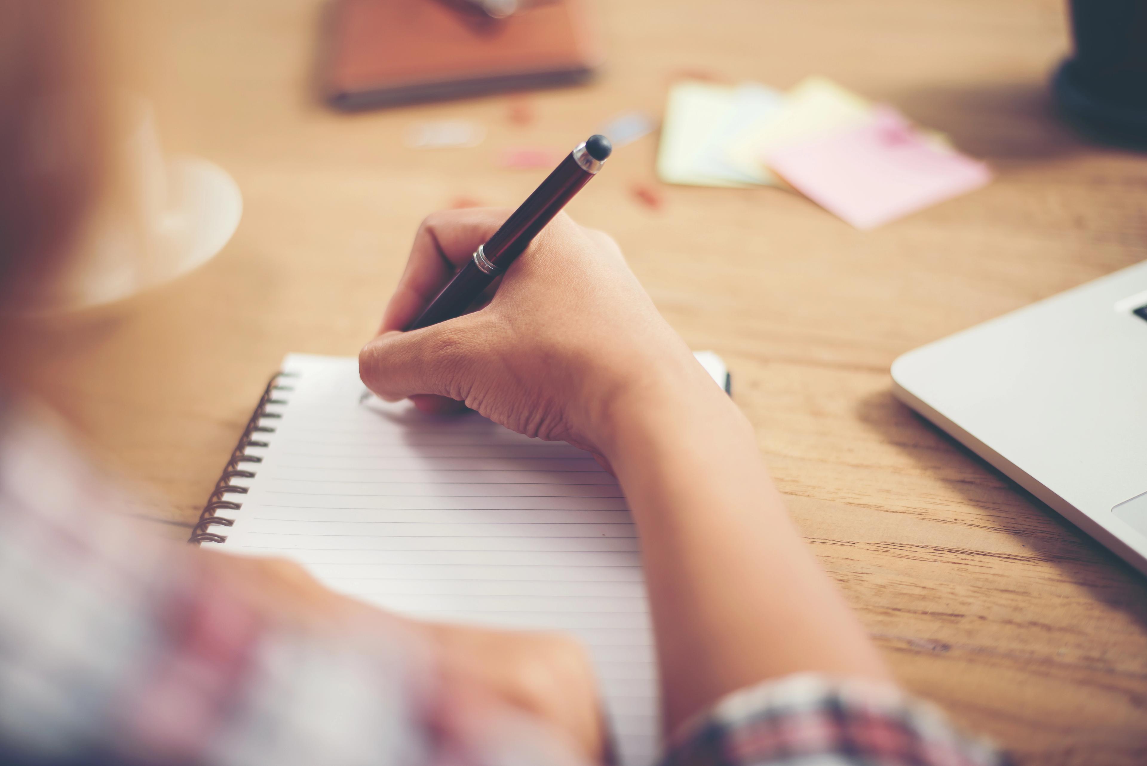 A hand holding a pen on an empty notebook, as a partner from a couple prepares to start the "Complete the Story" Game, which is one f the best indoor Christmas ideas for adults.