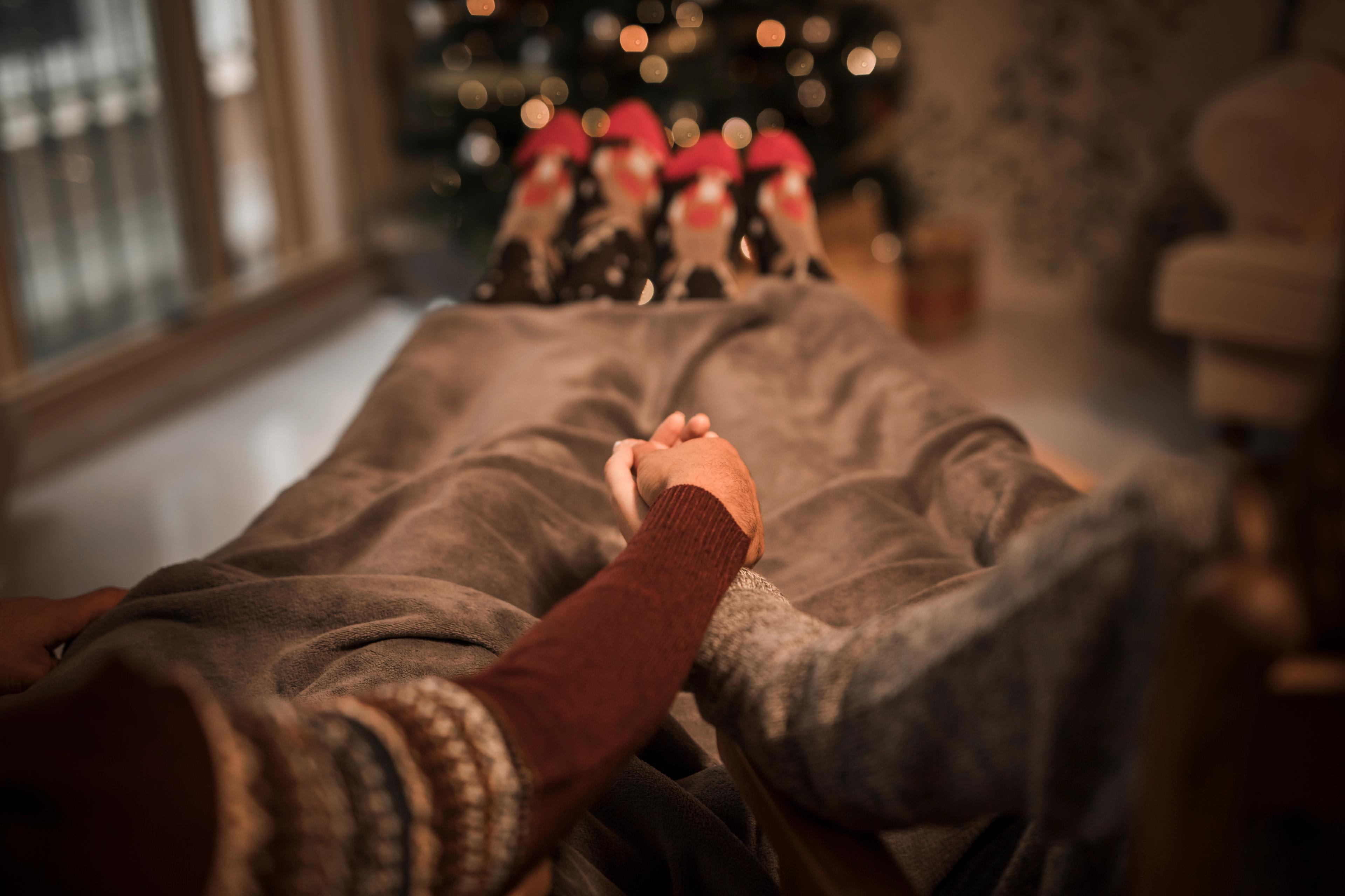 A couple cozied up in a blanket while watching a Christmas move near a decorated Christmas tree, which represents one of the best indoor Christmas games ideas for adults.