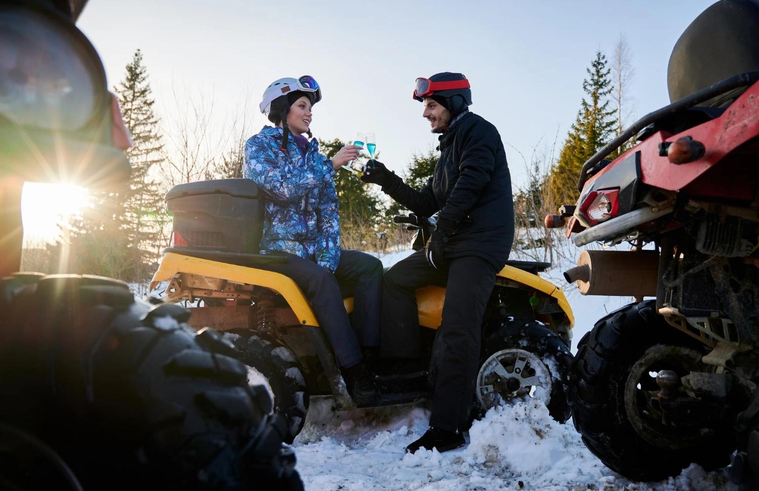 A couple toasting on an ATV after going on an adventure through the snowy forest, which is one of the best outdoor activities for couples.