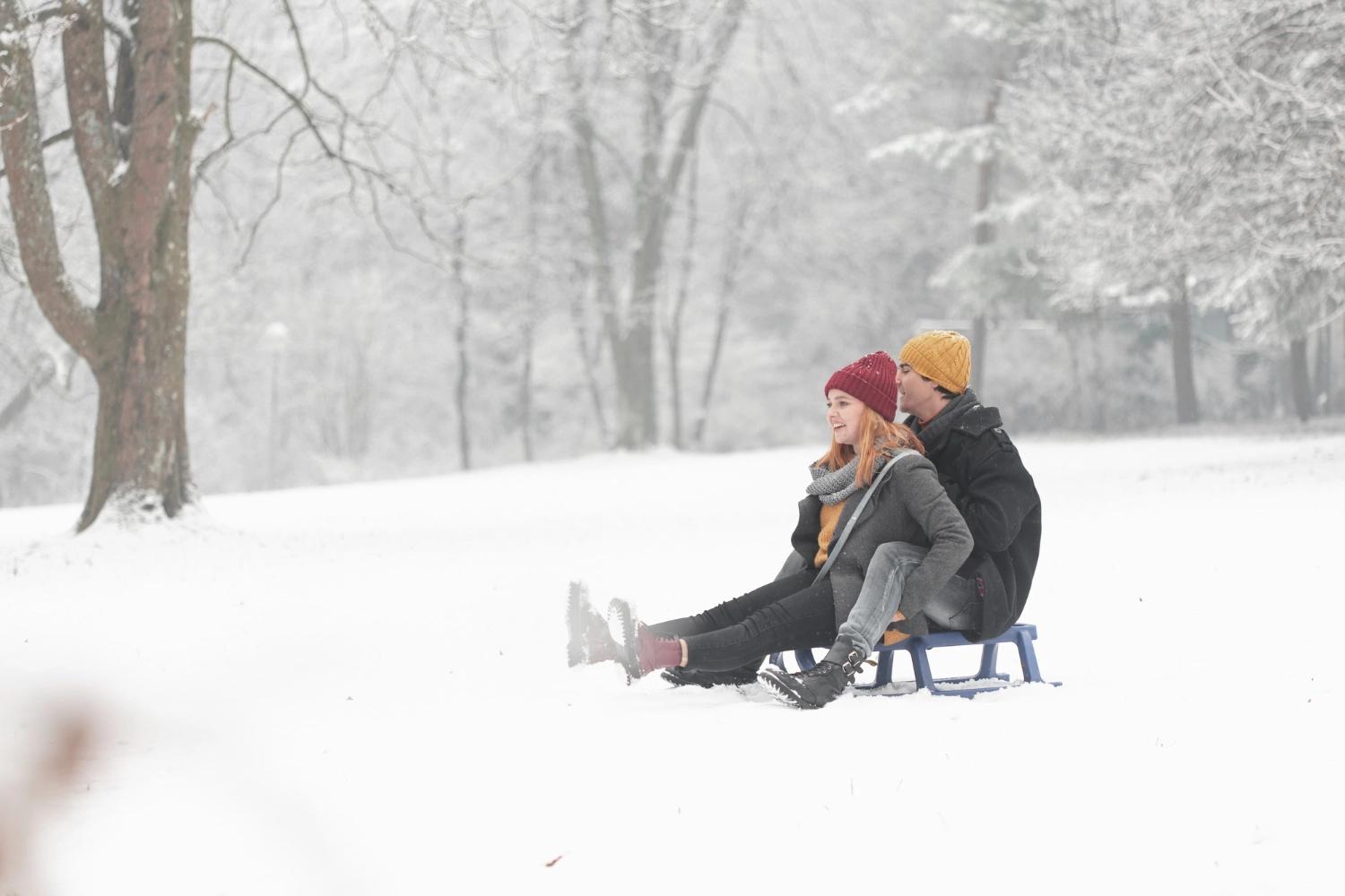 A couple going sledding in a snowy park, which is one of the best outdoor activities for couples.
