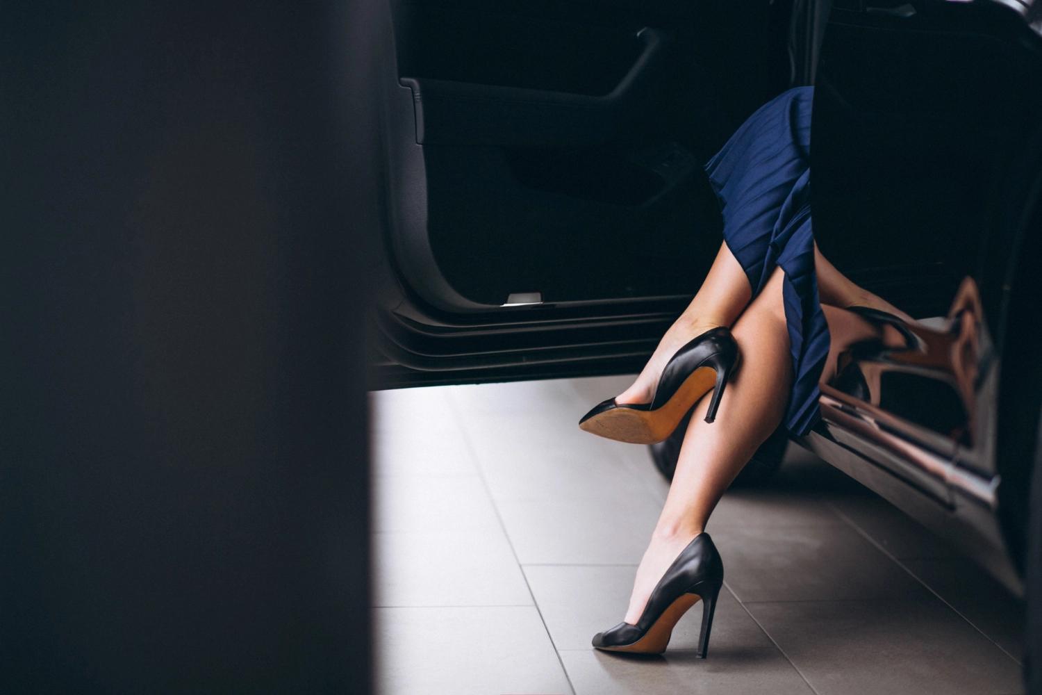 A woman getting out of the car and showing her black, elegant high heels, which is considered one of the major turn ons.