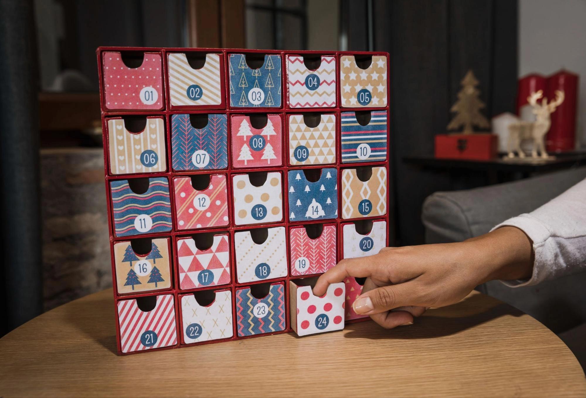 A picture of a wooden advent calendar and a hand opening an entry, which is one of the best  winter date activities for couples in a long distance relationship.