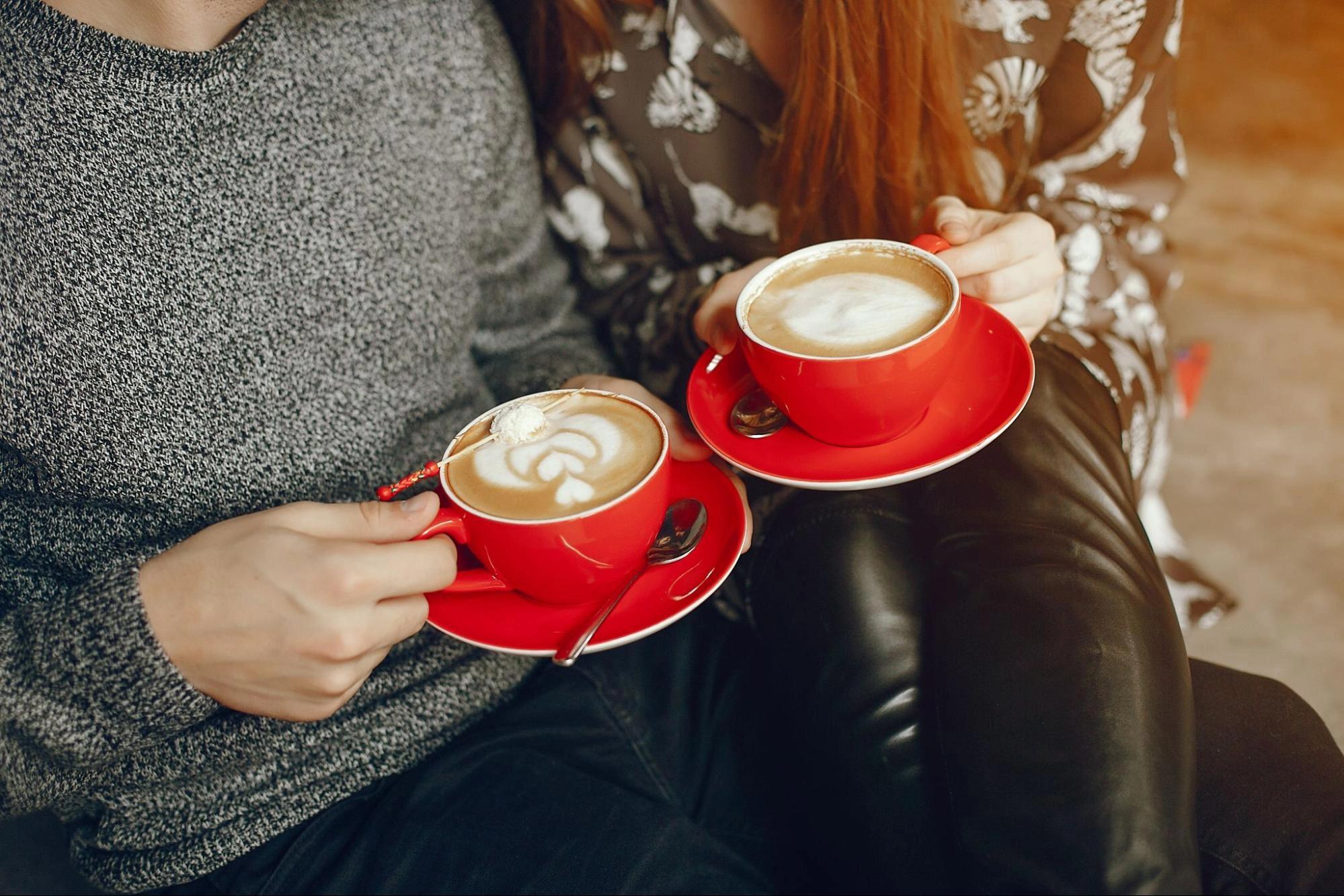 A couple holding two cups of coffees, dressed in warm, winter clothes, which is one of the best winter date activities for couples.