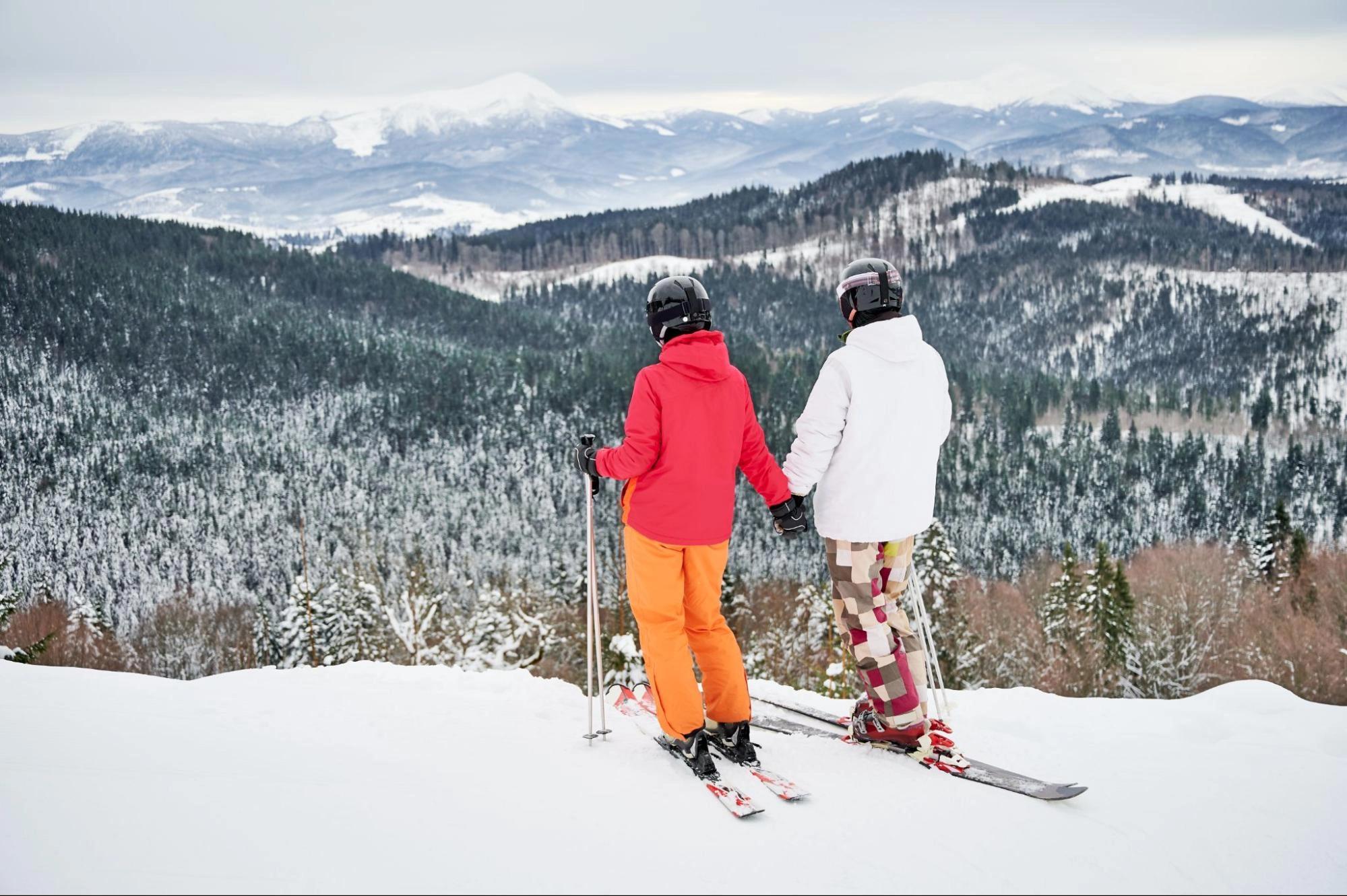 A couple overlooking a snowy mountain while skiing, which is one of the best expensive winter date activities for couples.