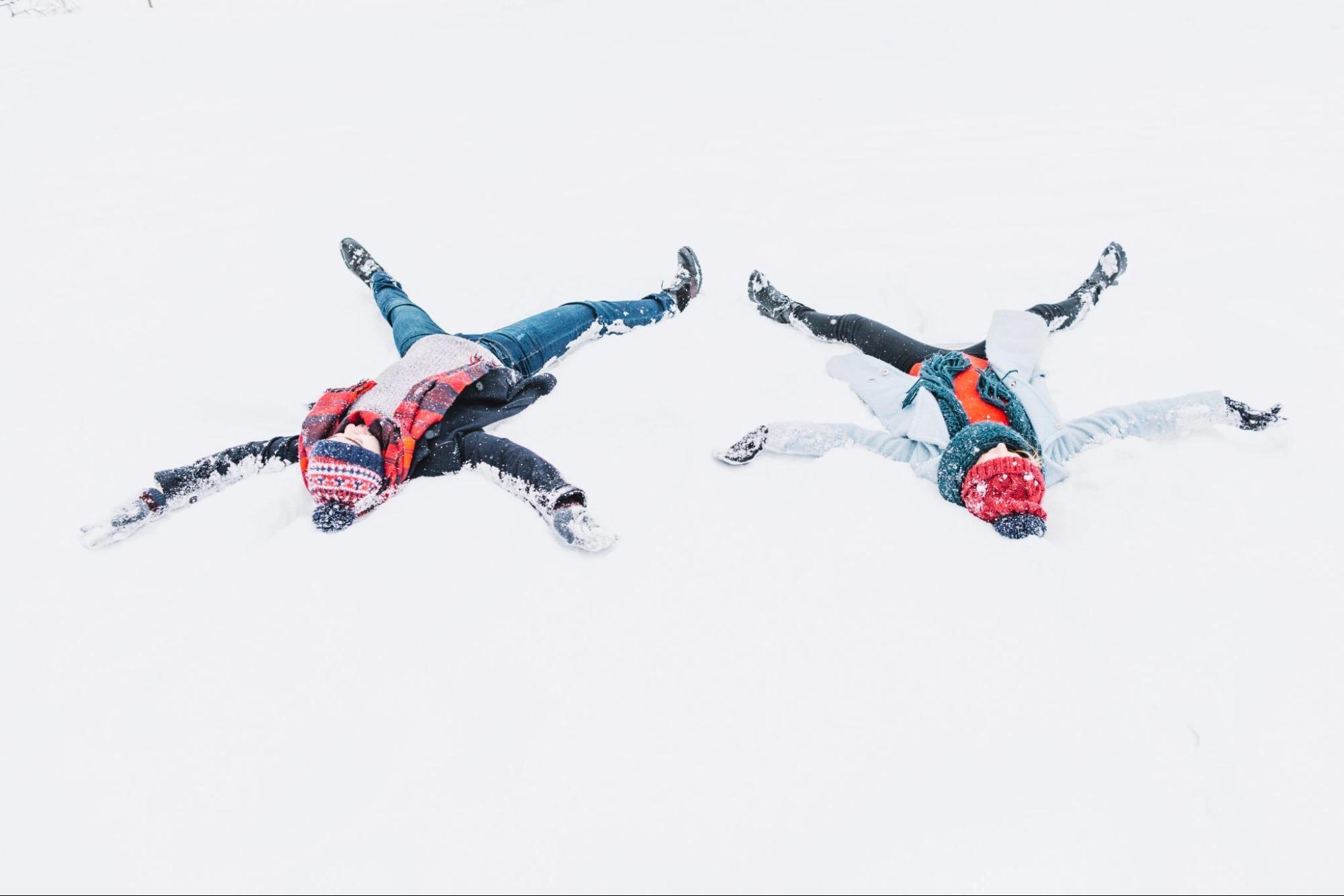 A couple doing snow angles in the snow, which is one of the best winter date activities for couples.