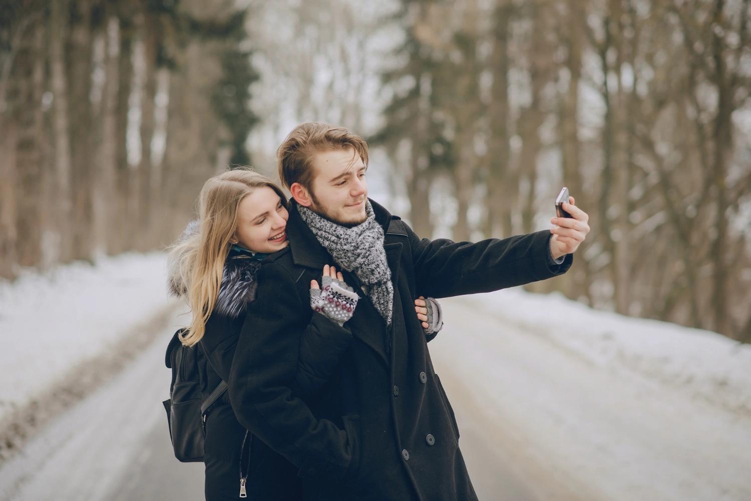 A couple taking a selfie that they will add on Couple Joy's app while on winter weekend getaways somewhere snowy.
